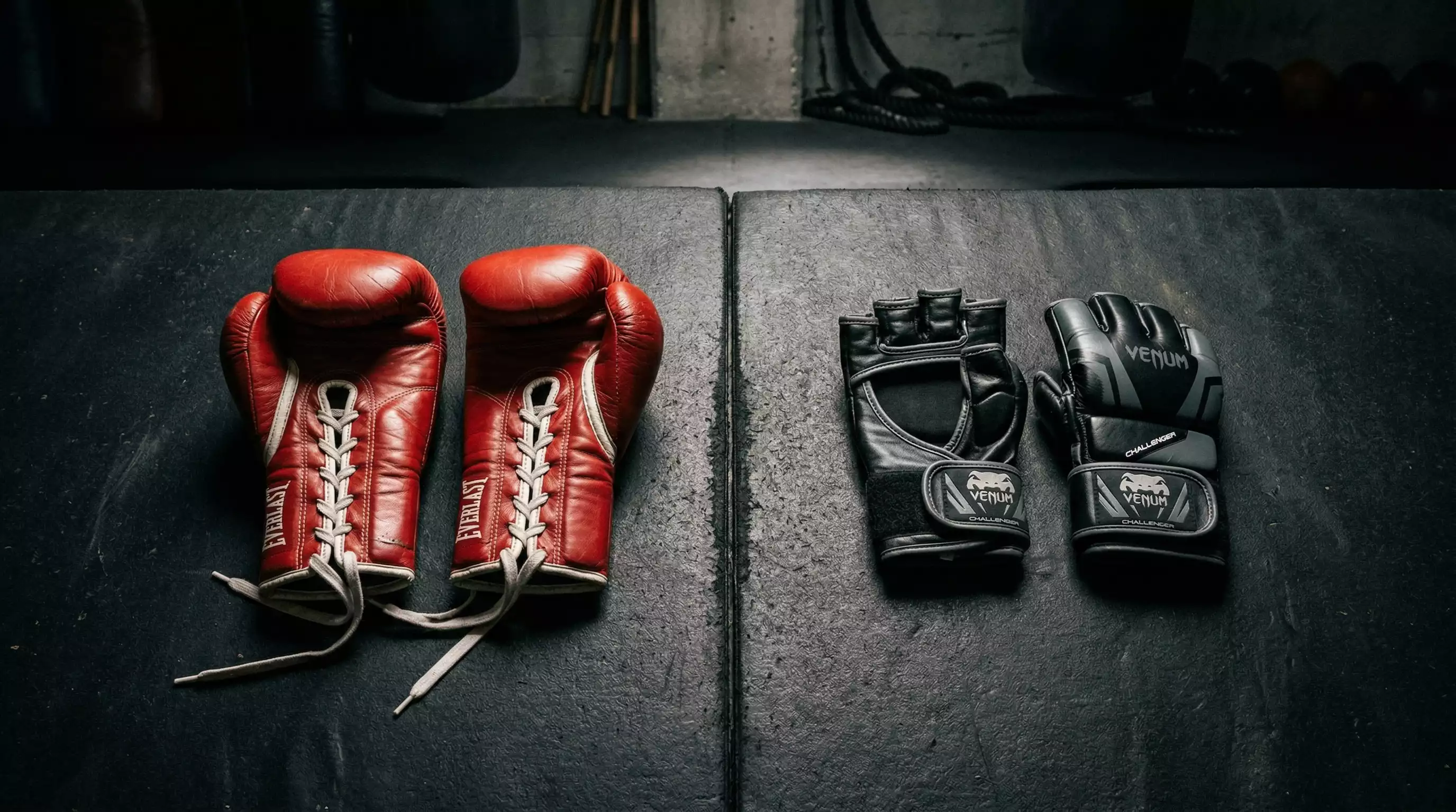 Boxring und Boxhandschuhe neben MMA-Handschuhen auf einer Trainingsmatte